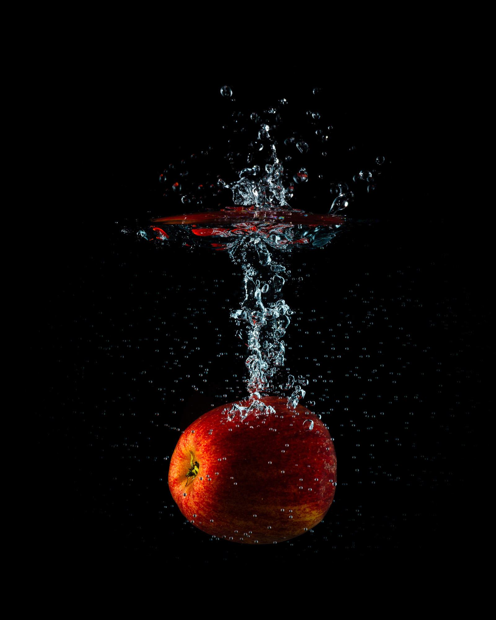 red apple splash in water, submerged, and with streak of bubbles rising