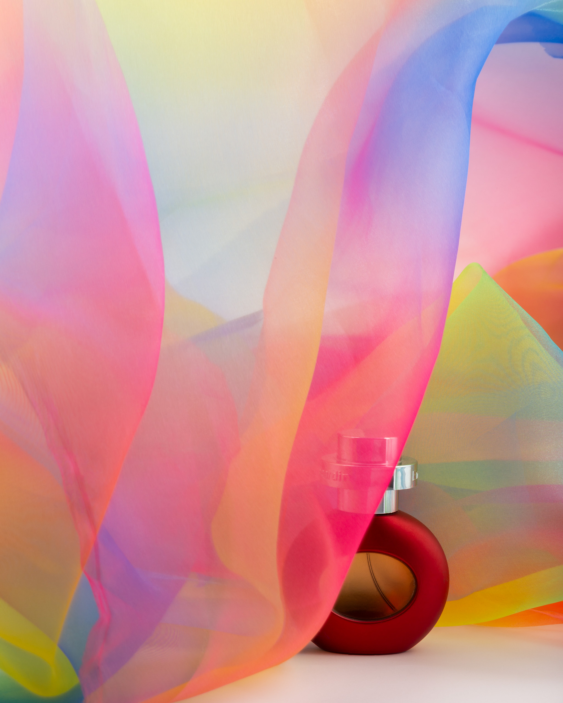 Red perfume bottle covered by flowing organza.