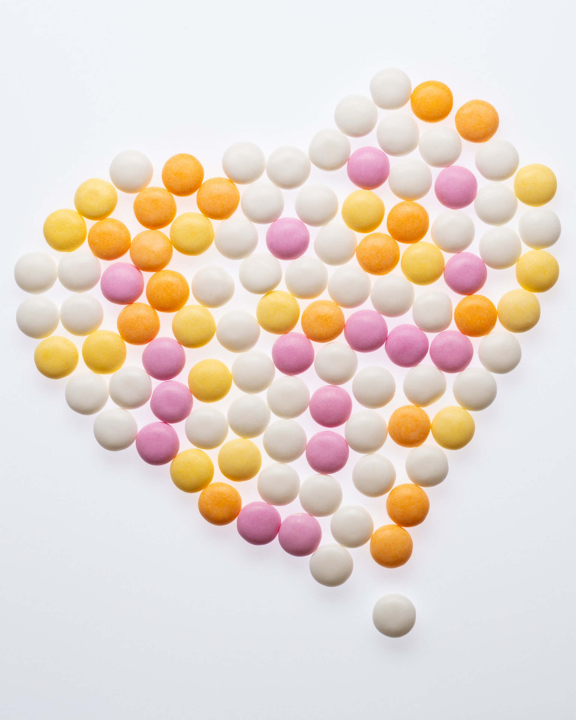 Colourful Mentos forming a heart shape on a bright background.