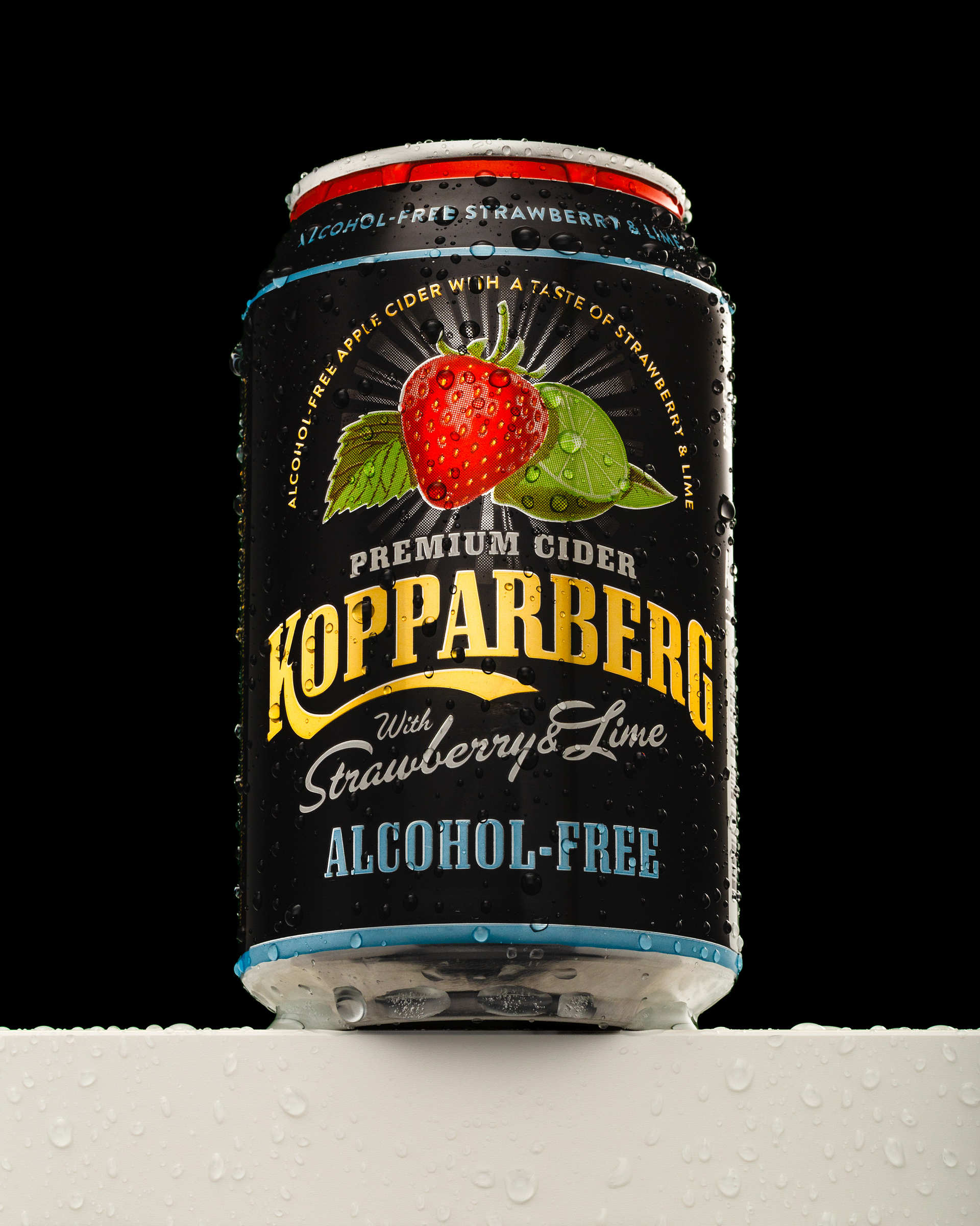 A black can of strawberry and lime alcohol-free cider stands on a white surface covered with water droplets against a black background.