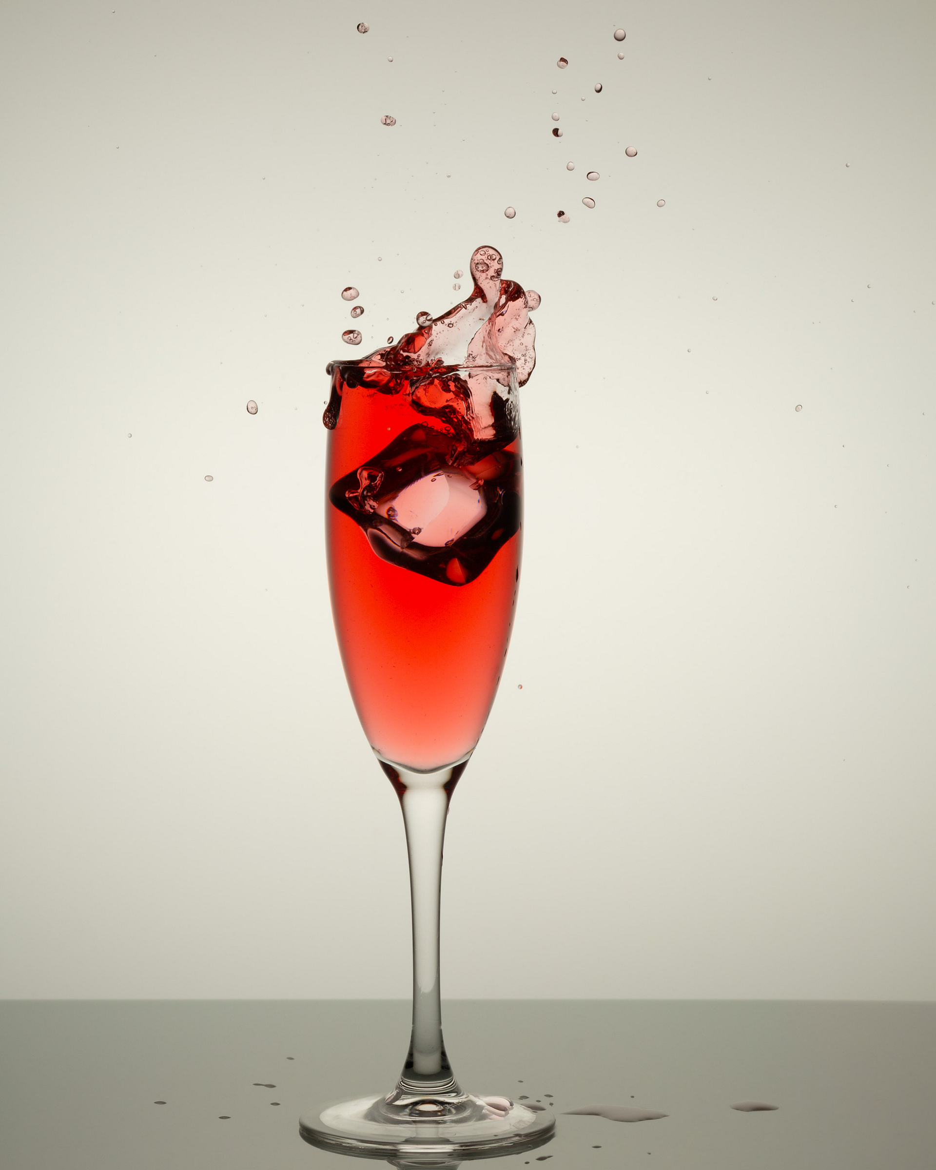 Glass with red liquid and an ice cube splash.