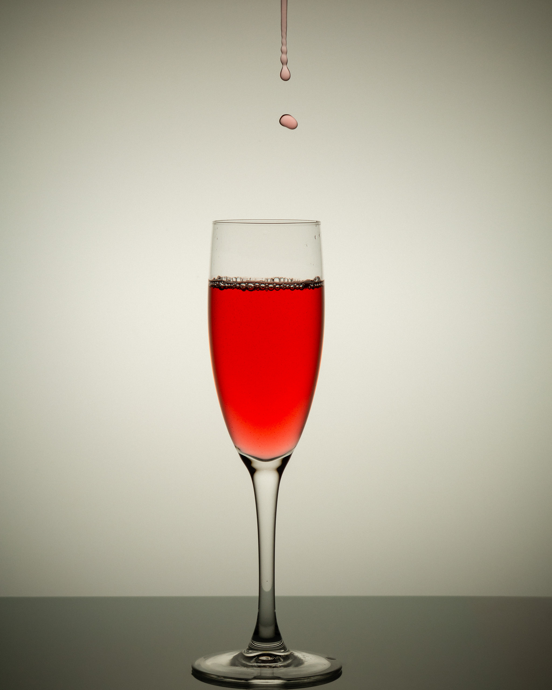 A glass filled with red liquid with droplets falling above it against a light