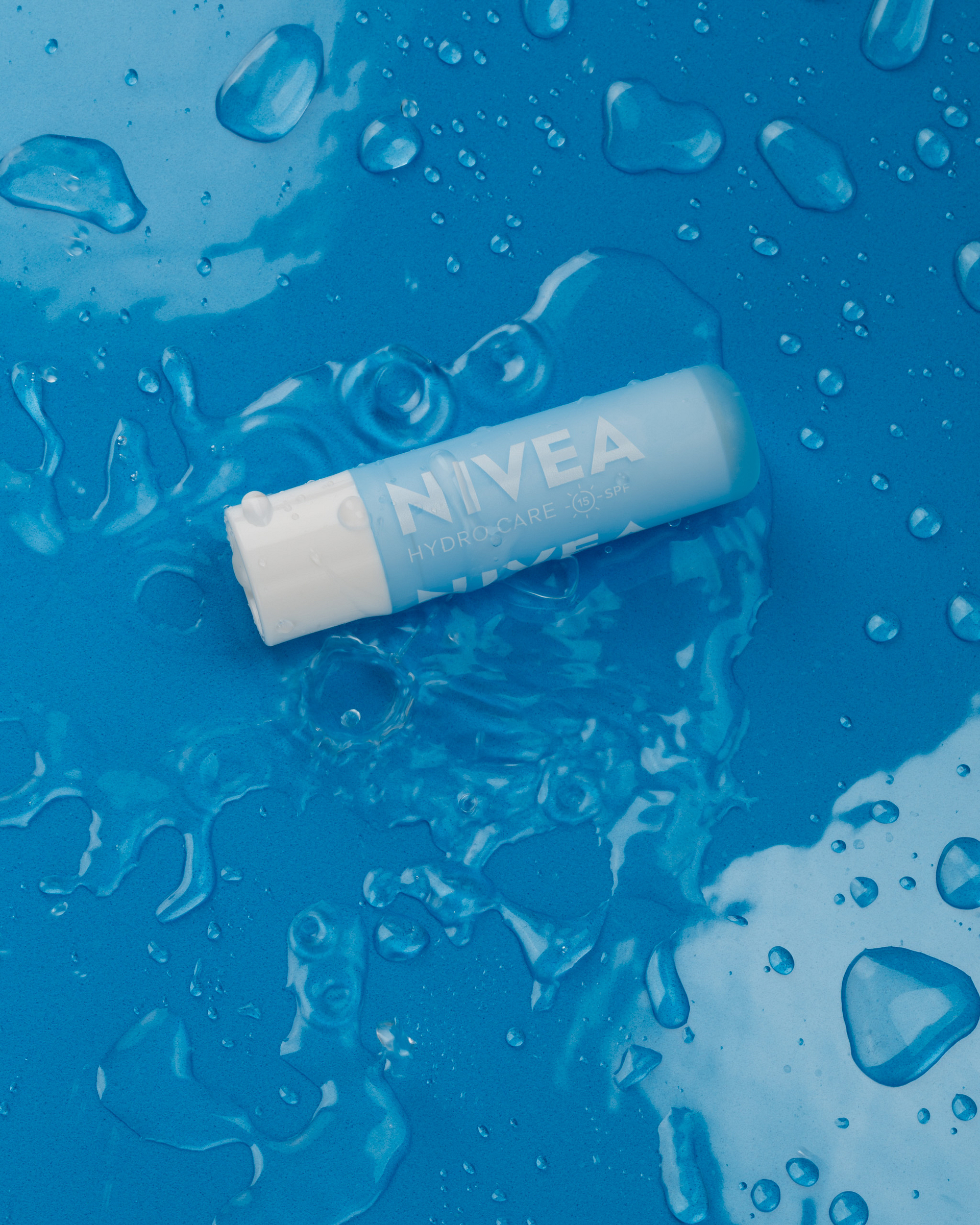Blue lip balm with water droplets on a blue background.