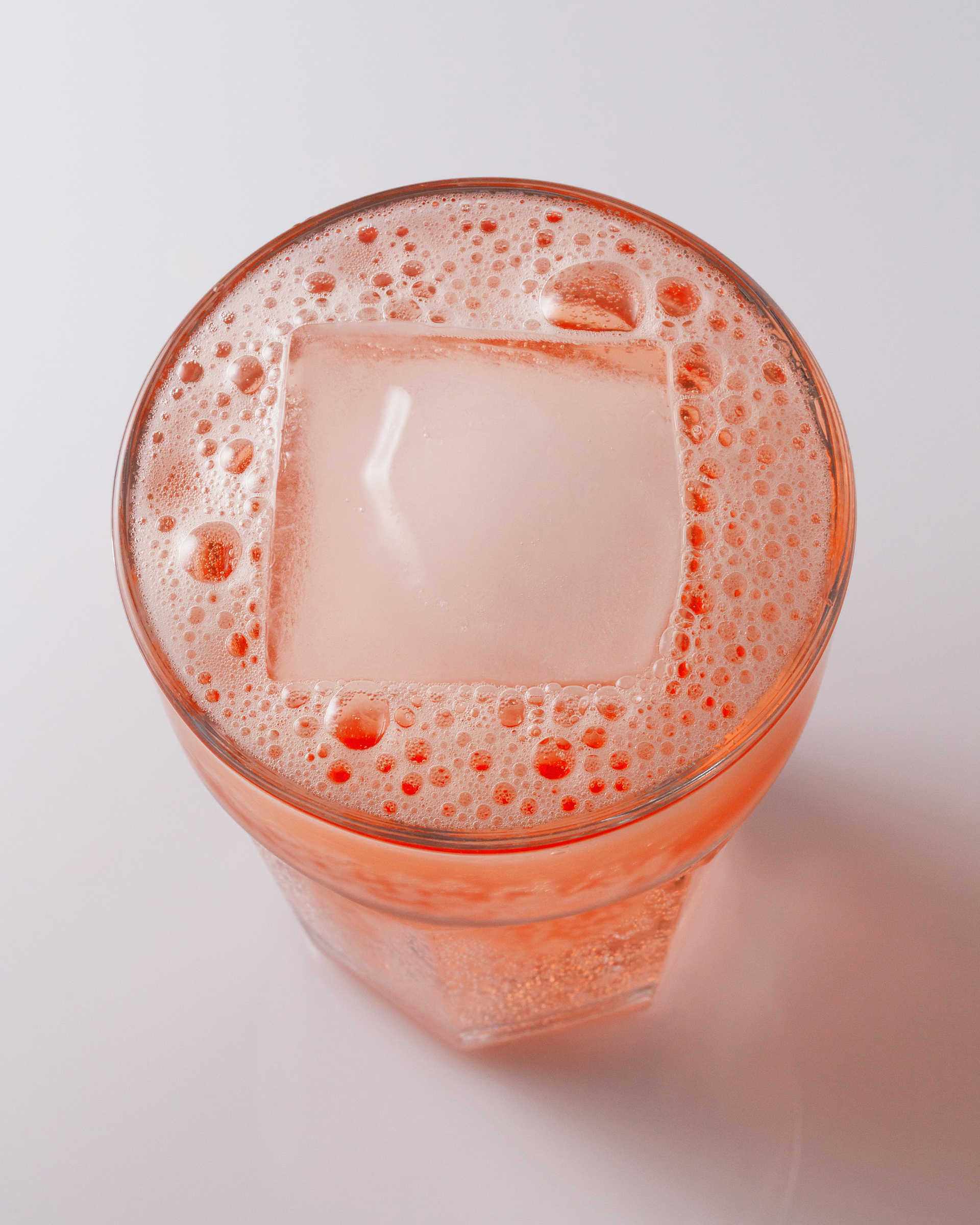 Top view of a drink with a square ice cube and bubbles.