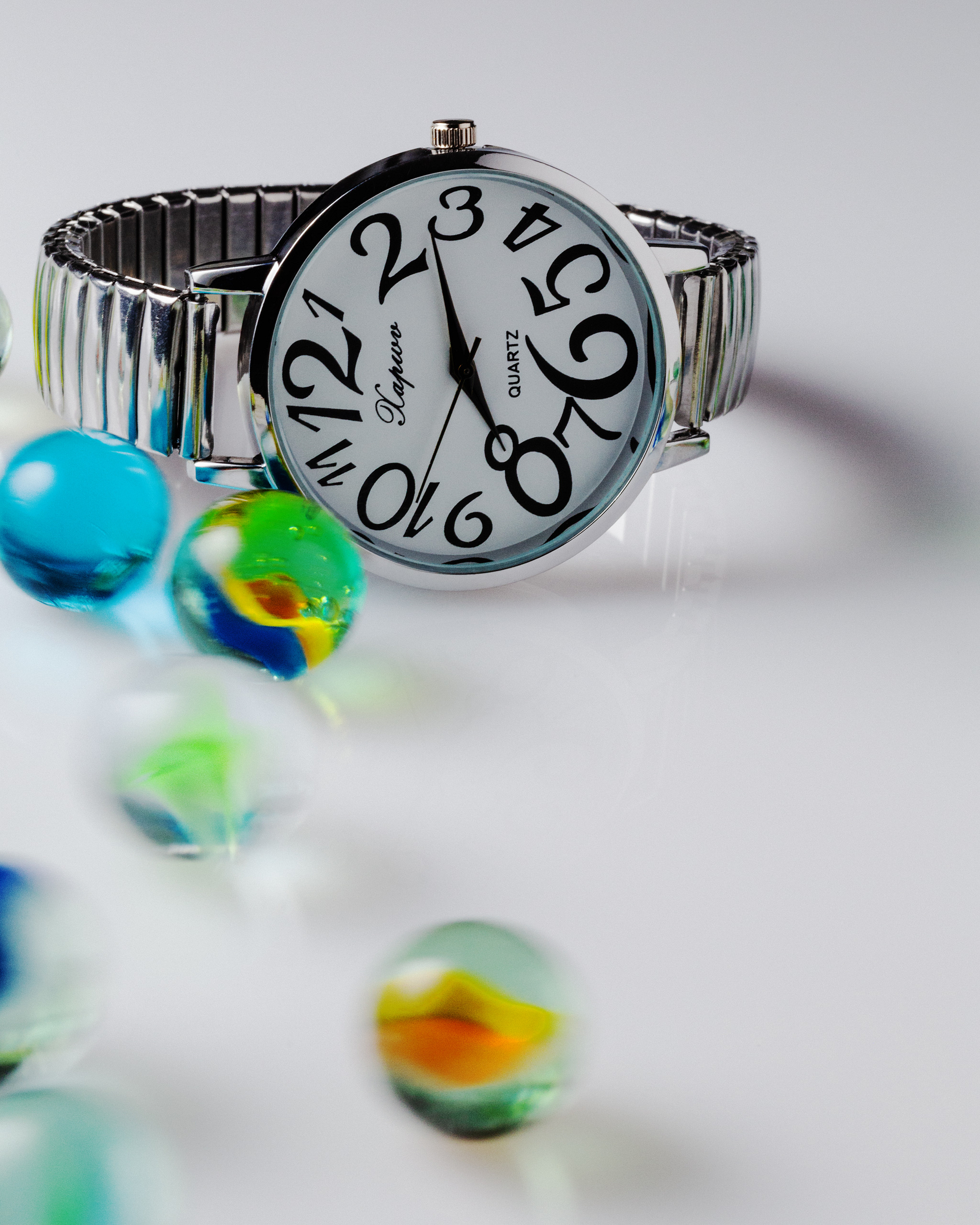 Chrome watch with marbles in movement on a bright grey background