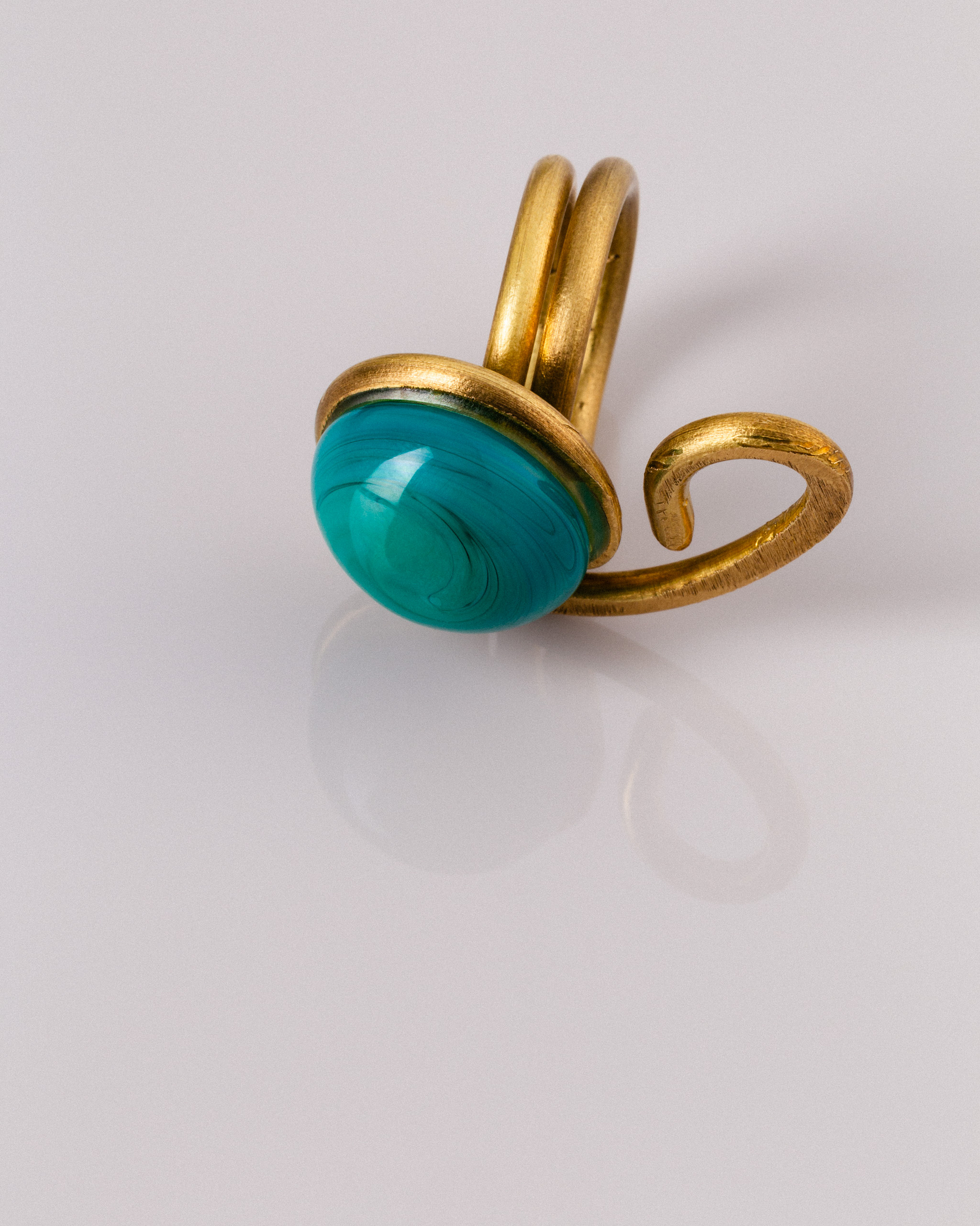A bronze ring with a green glass stone against a light background.
