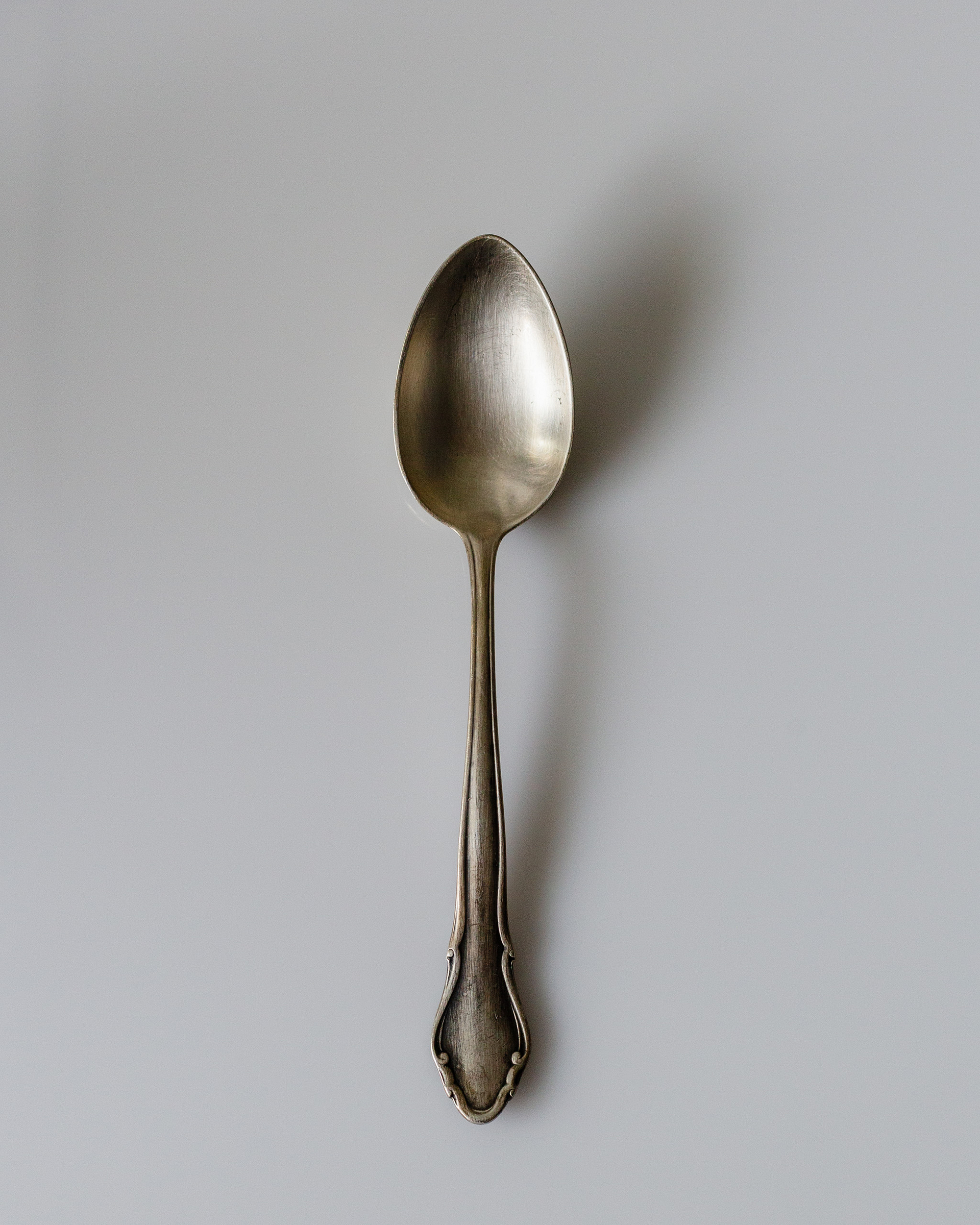 antique silver spoon on grey background pointing up with a shadow