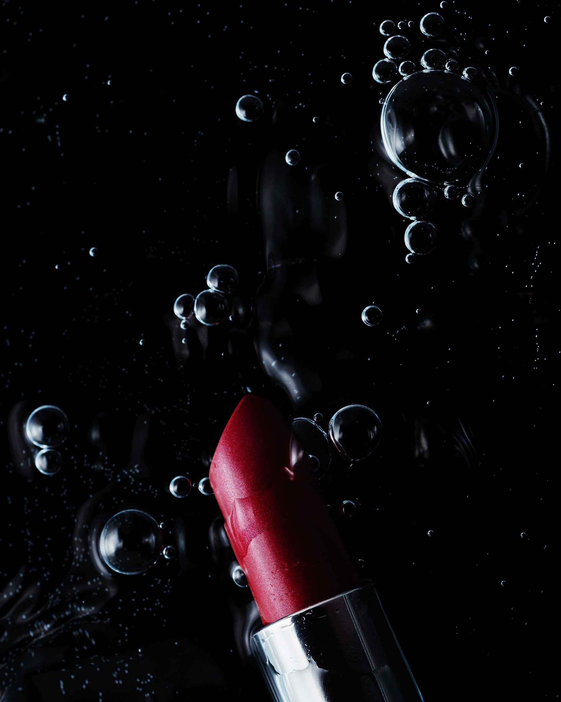 A red lipstick in water with bubbles on a dark background.